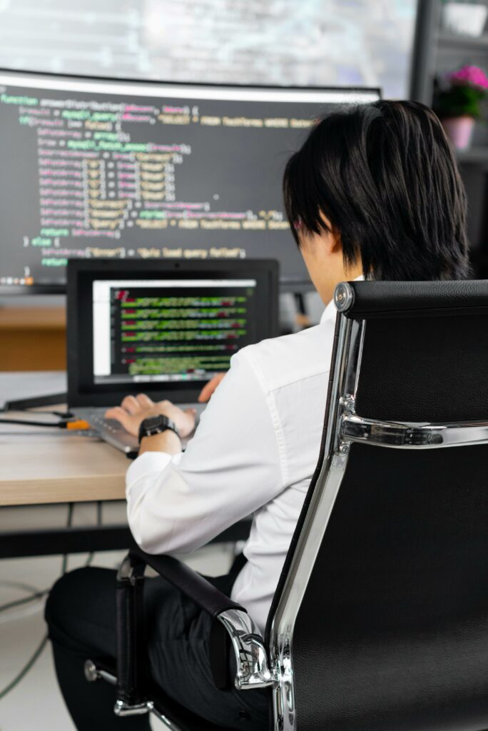 Professional software developer writing code at a desk in a modern office environment.